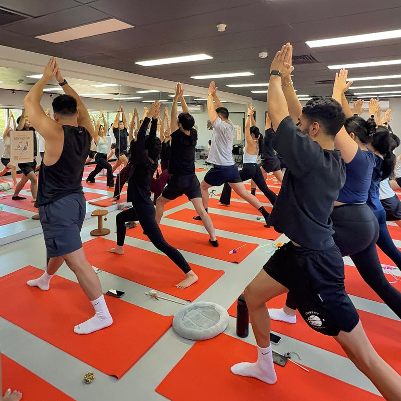 Group of people practicing kitty yoga in a room with orange mats and mirrors on the wall in Sydney