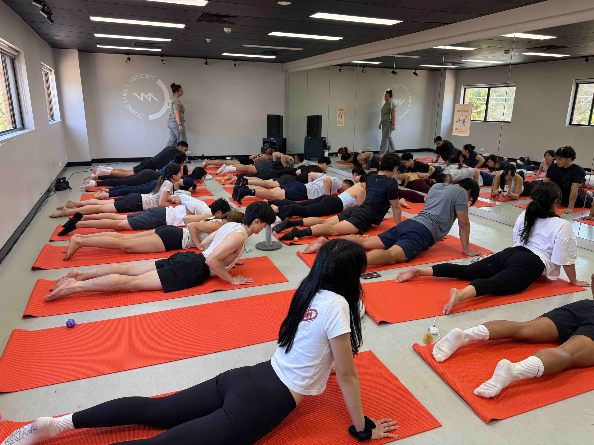 Group of people practicing kitty yoga in a room with orange mats and mirrors on the wall in Sydney